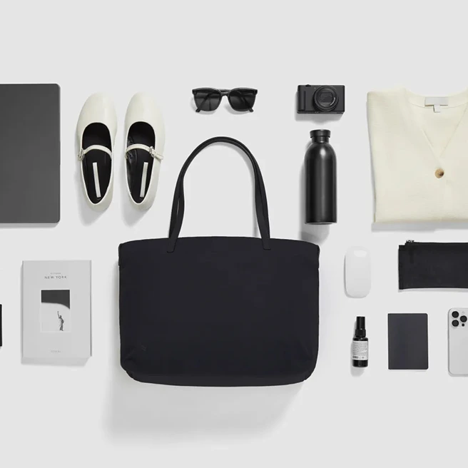 A flat-lay arrangement of everyday items centered around a black LOJEL Semo tote.